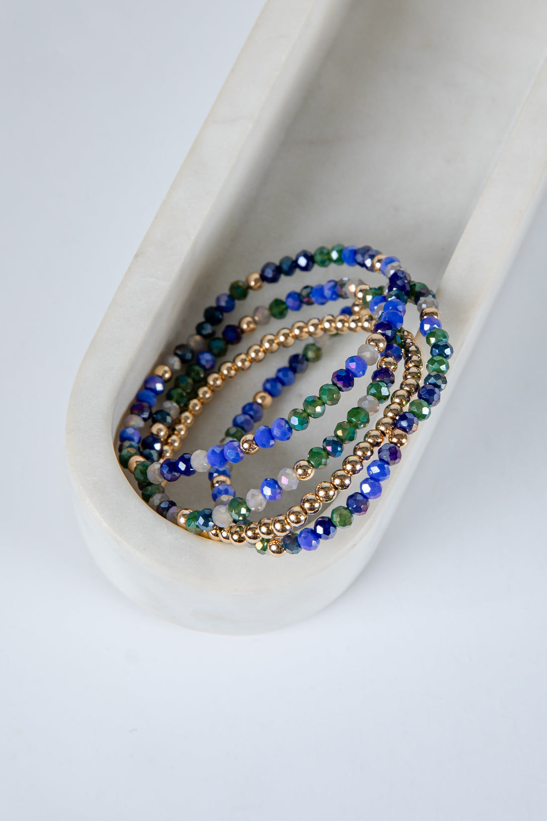Set of beaded bracelets in blue, green, and gold on a white dish.