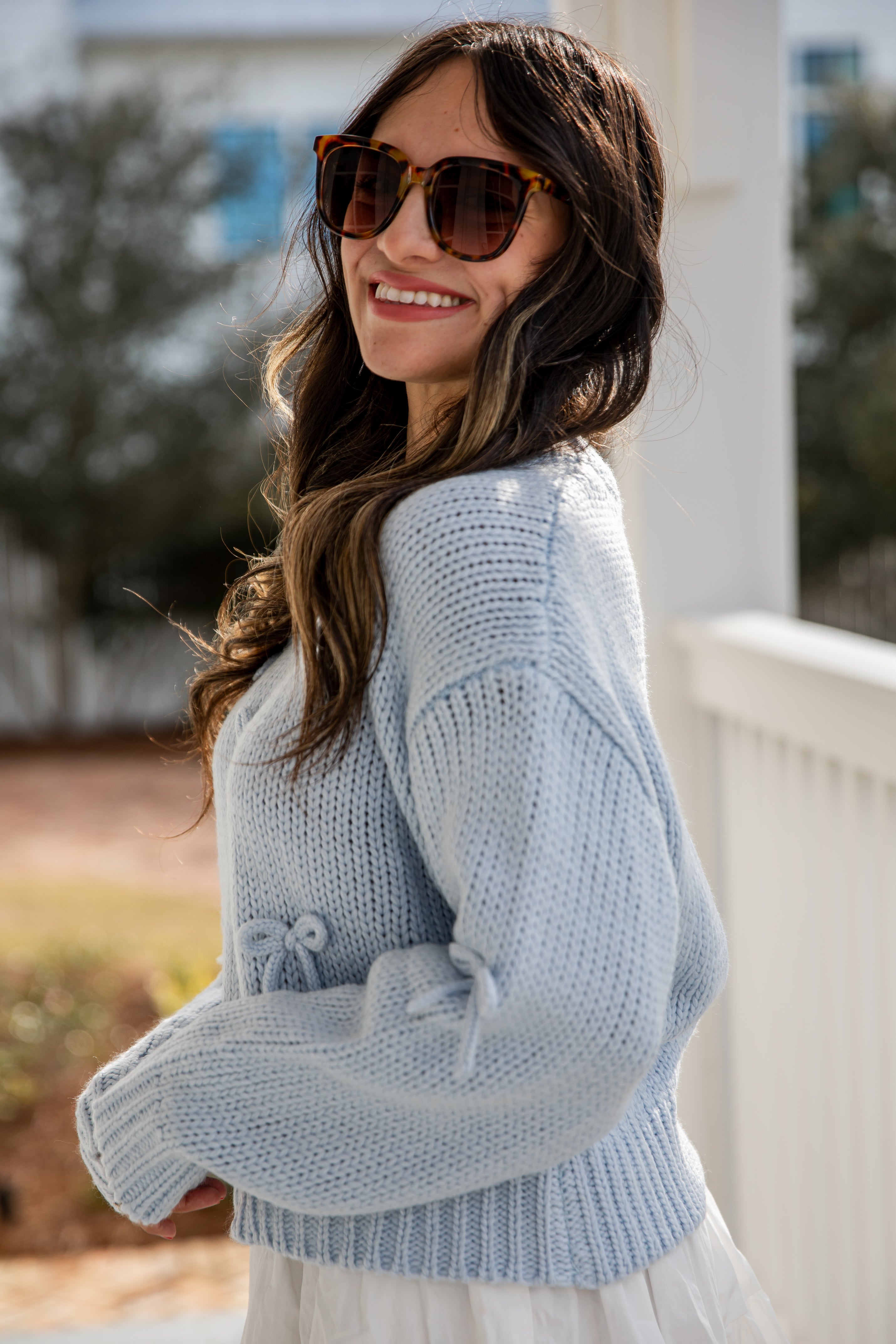 Woman wearing a light blue knitted cardigan and sunglasses outdoors.