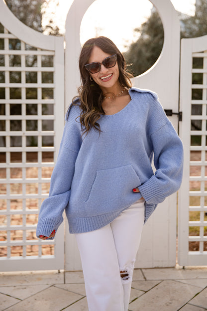 Woman wearing a light blue sweater and white pants standing in front of a decorative white archway.