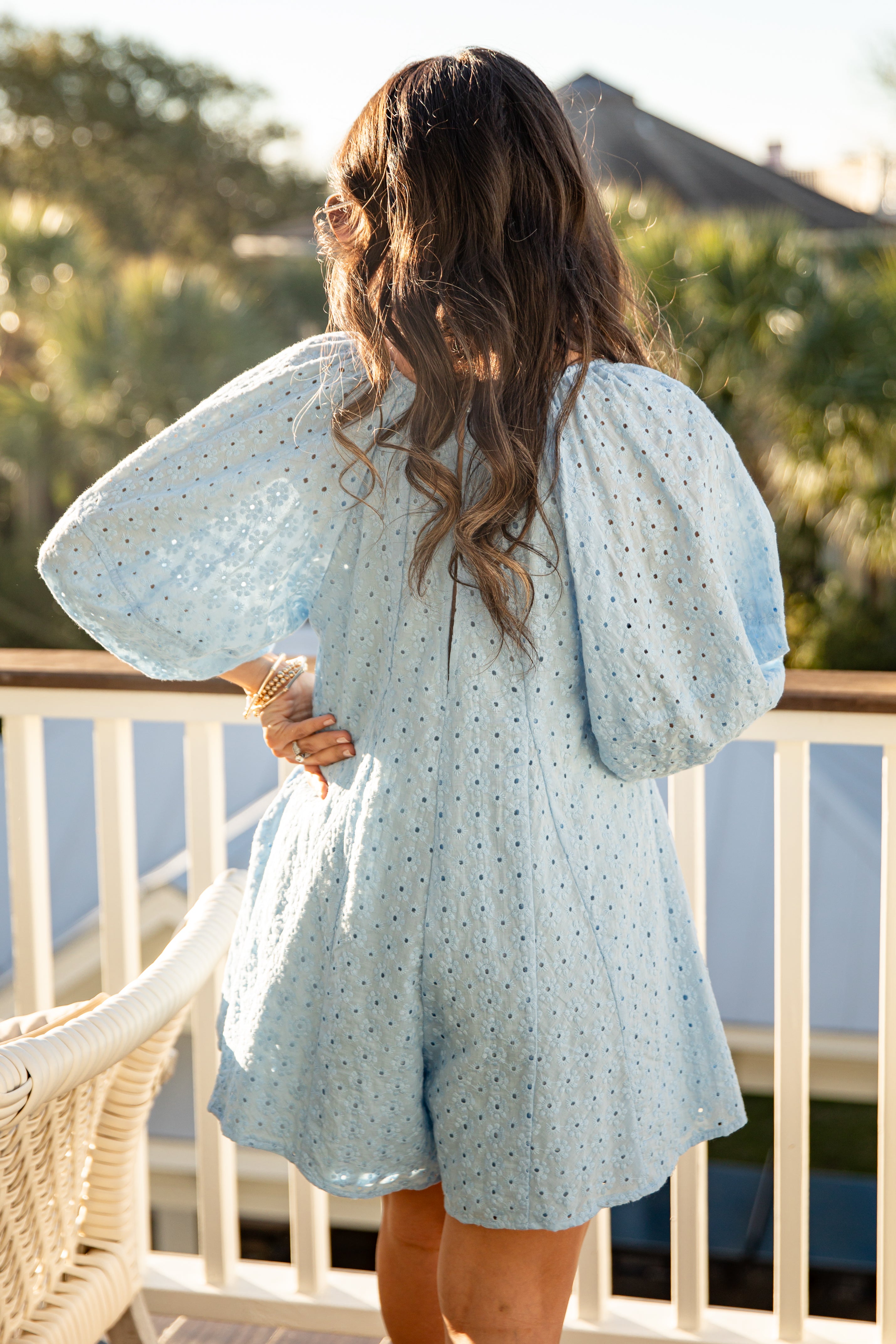Woman wearing a light blue floral dress on a balcony with a blurred outdoor background