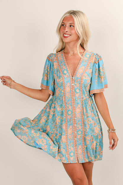 Woman wearing a blue and orange floral dress against a plain background