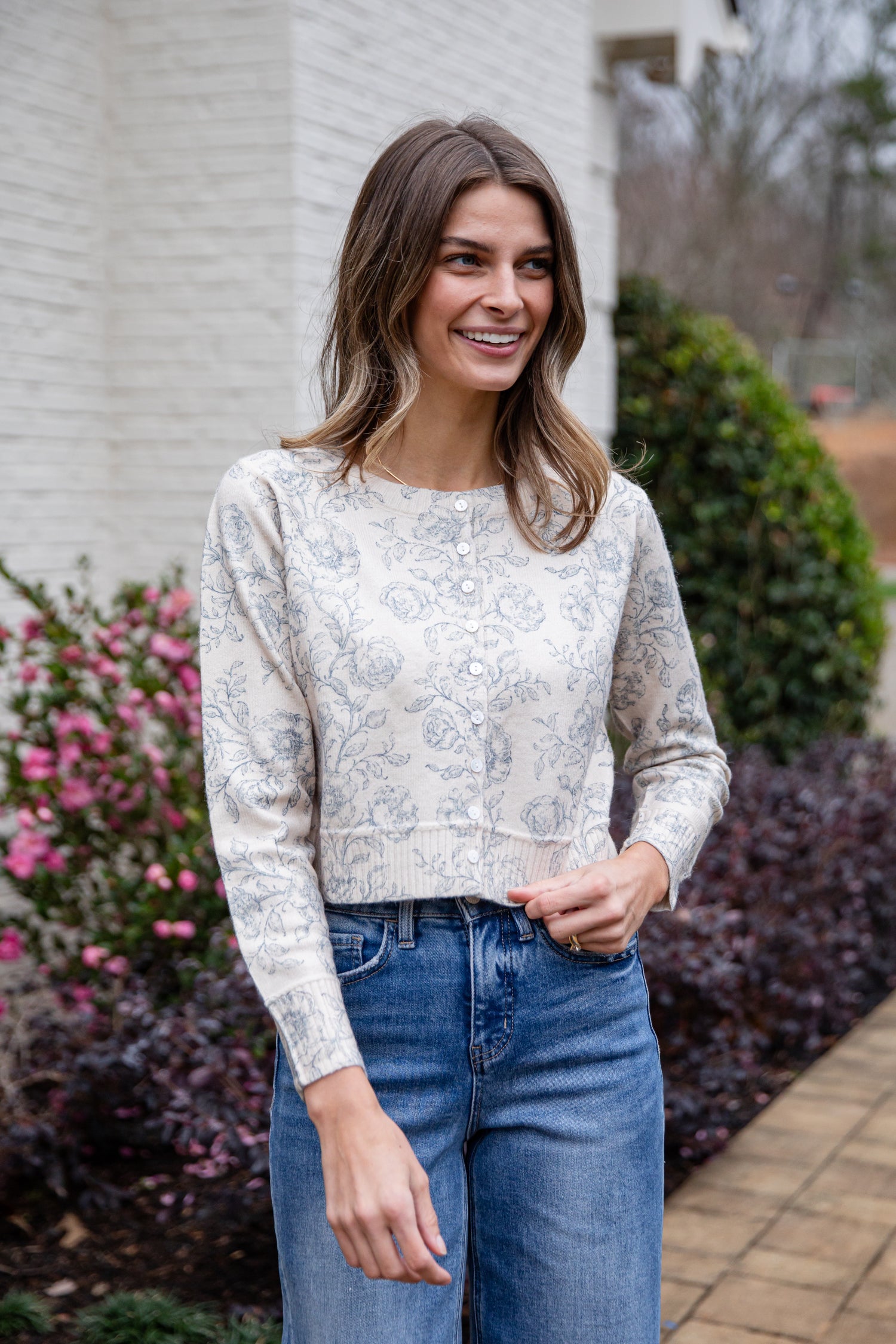 Woman wearing a floral sweater and blue jeans standing outdoors.