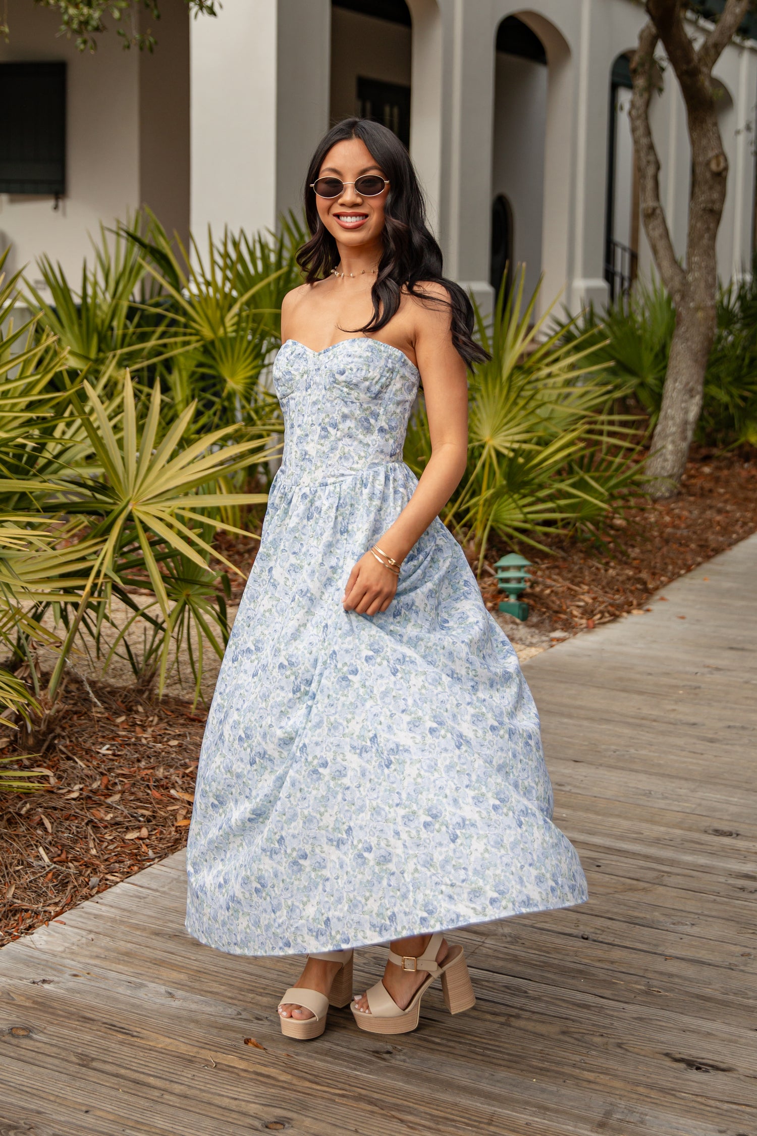 Woman in a floral dress standing on a wooden path with plants in the background