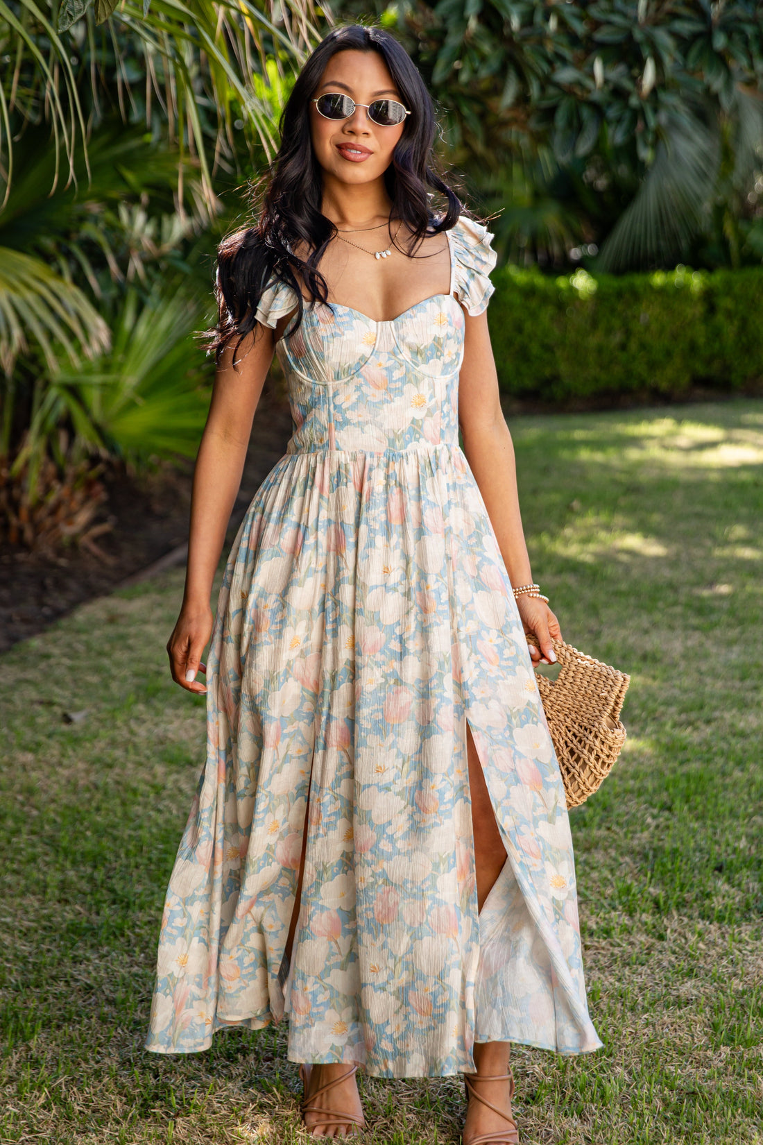 Woman in a floral dress standing outdoors with greenery in the background