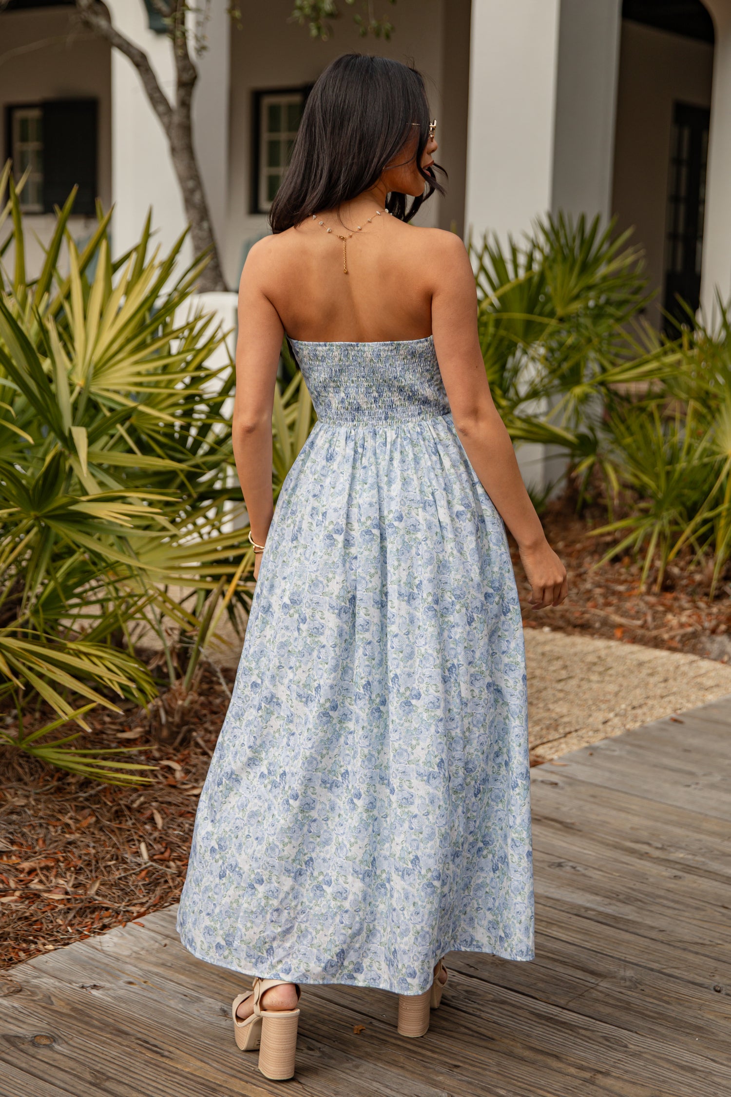 Woman in a floral dress standing on a wooden deck with plants in the background