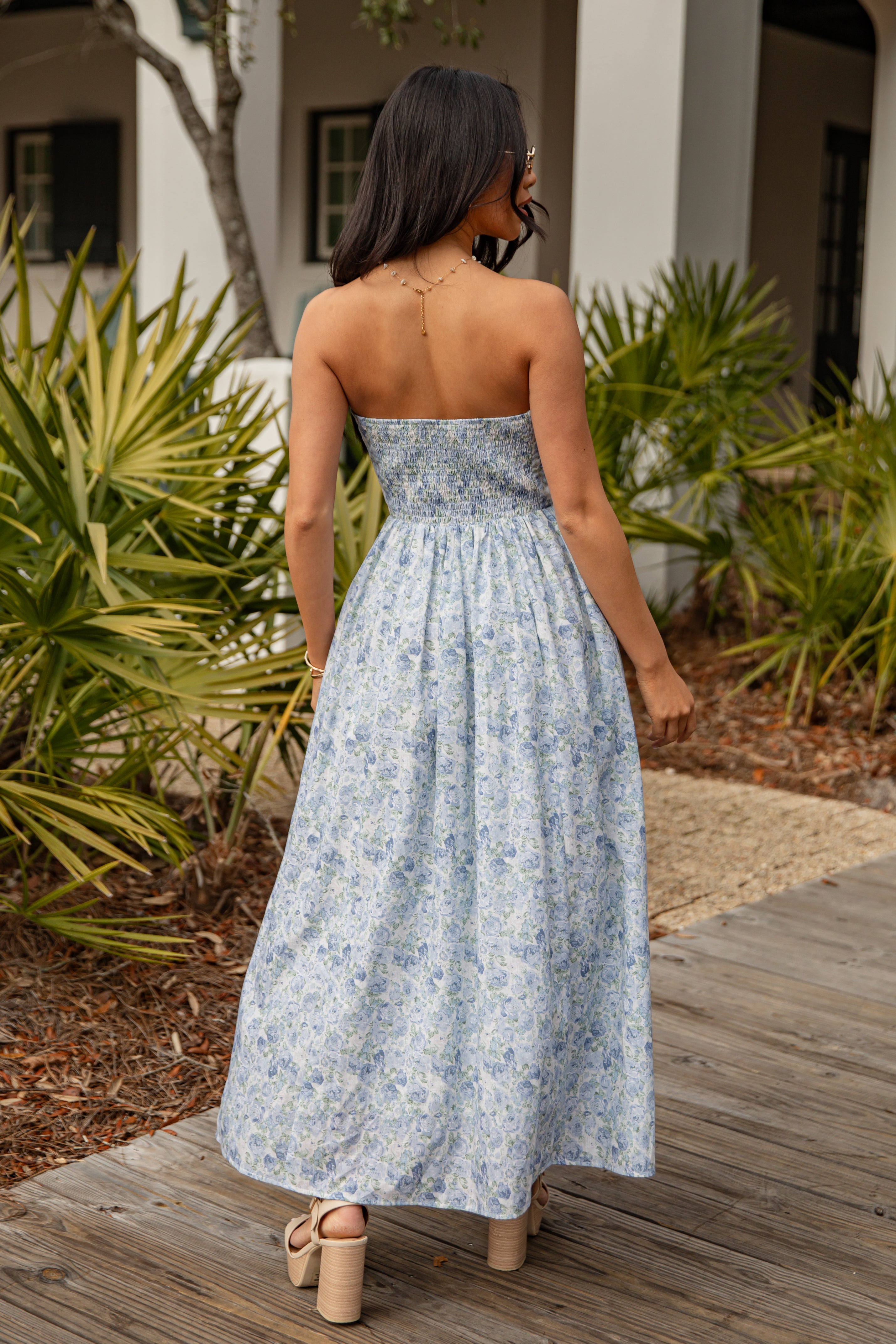 Woman in a floral dress standing on a wooden deck with plants in the background