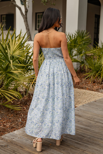 Woman in a floral dress standing on a wooden deck with plants in the background