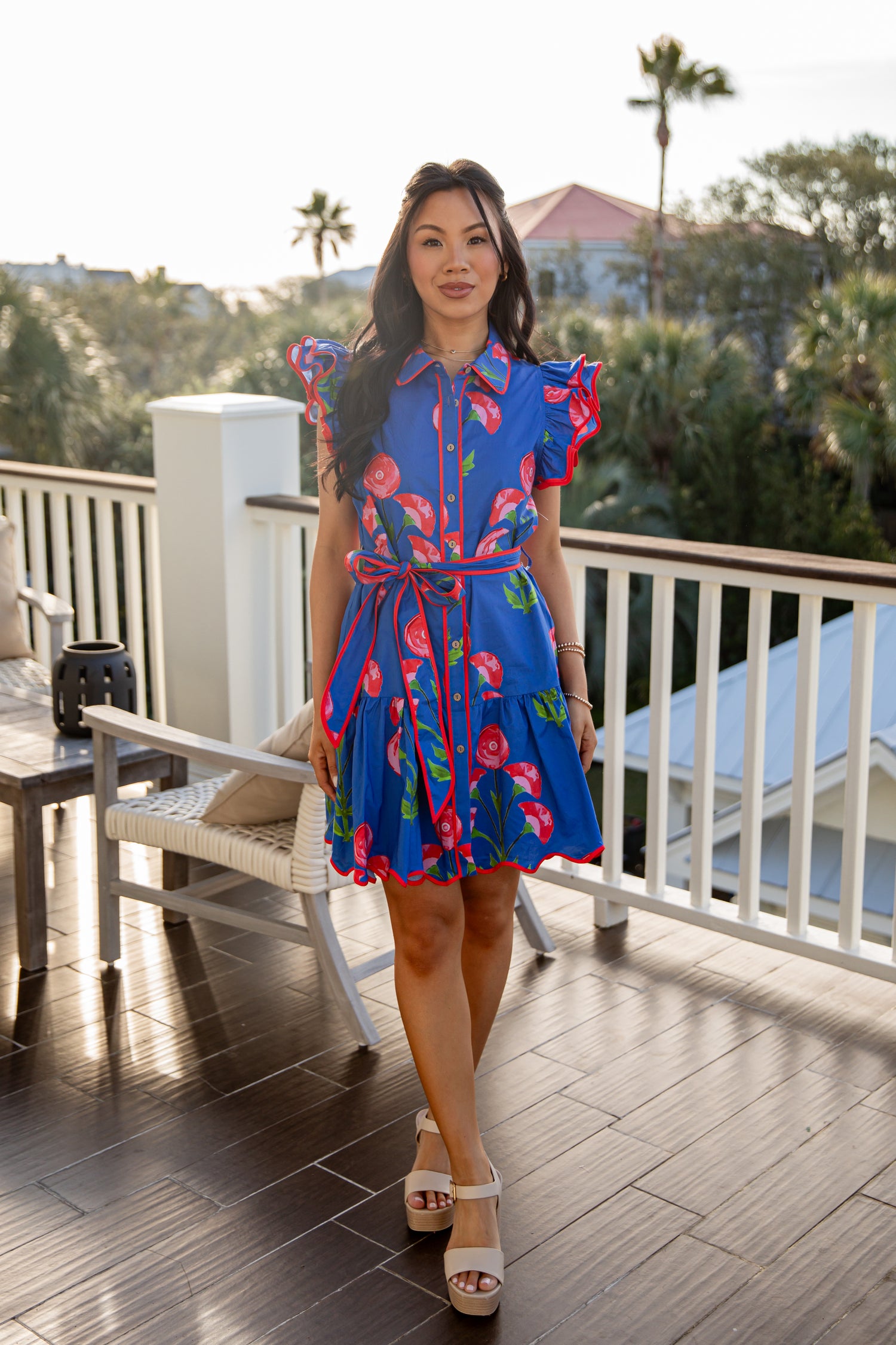 Woman in a blue floral dress standing on a patio with palm trees in the background