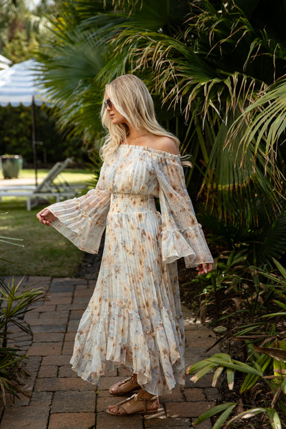 Woman in a floral off-shoulder dress standing outdoors with greenery around