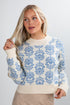 Woman wearing a white sweater with blue floral patterns against a plain background