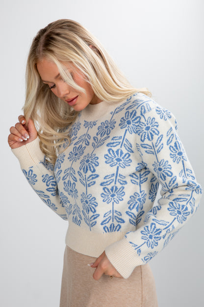 Woman wearing a white sweater with blue floral patterns on a plain background