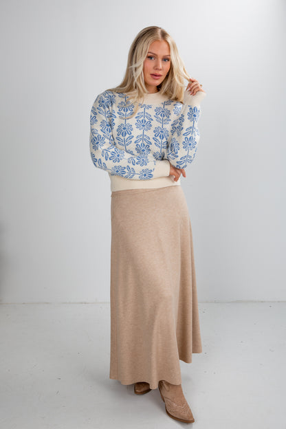 Woman wearing a floral sweater and beige skirt on a white background