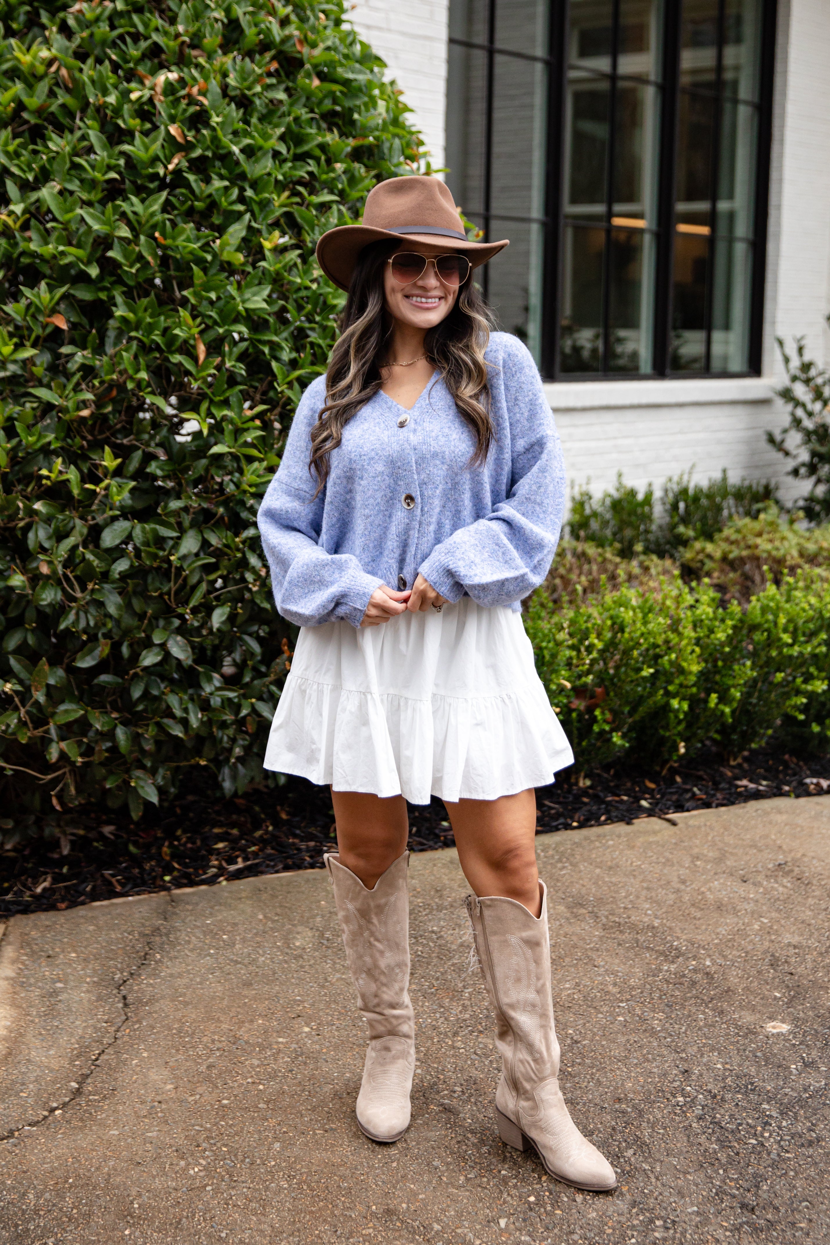 Woman wearing a blue sweater, white skirt, and beige knee-high boots standing outdoors.