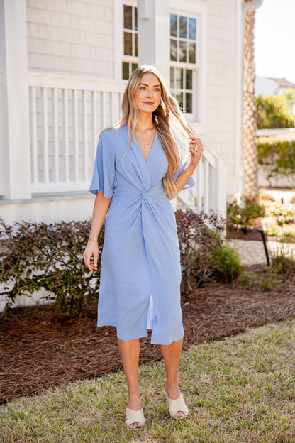 Woman in a blue dress standing outdoors near a house