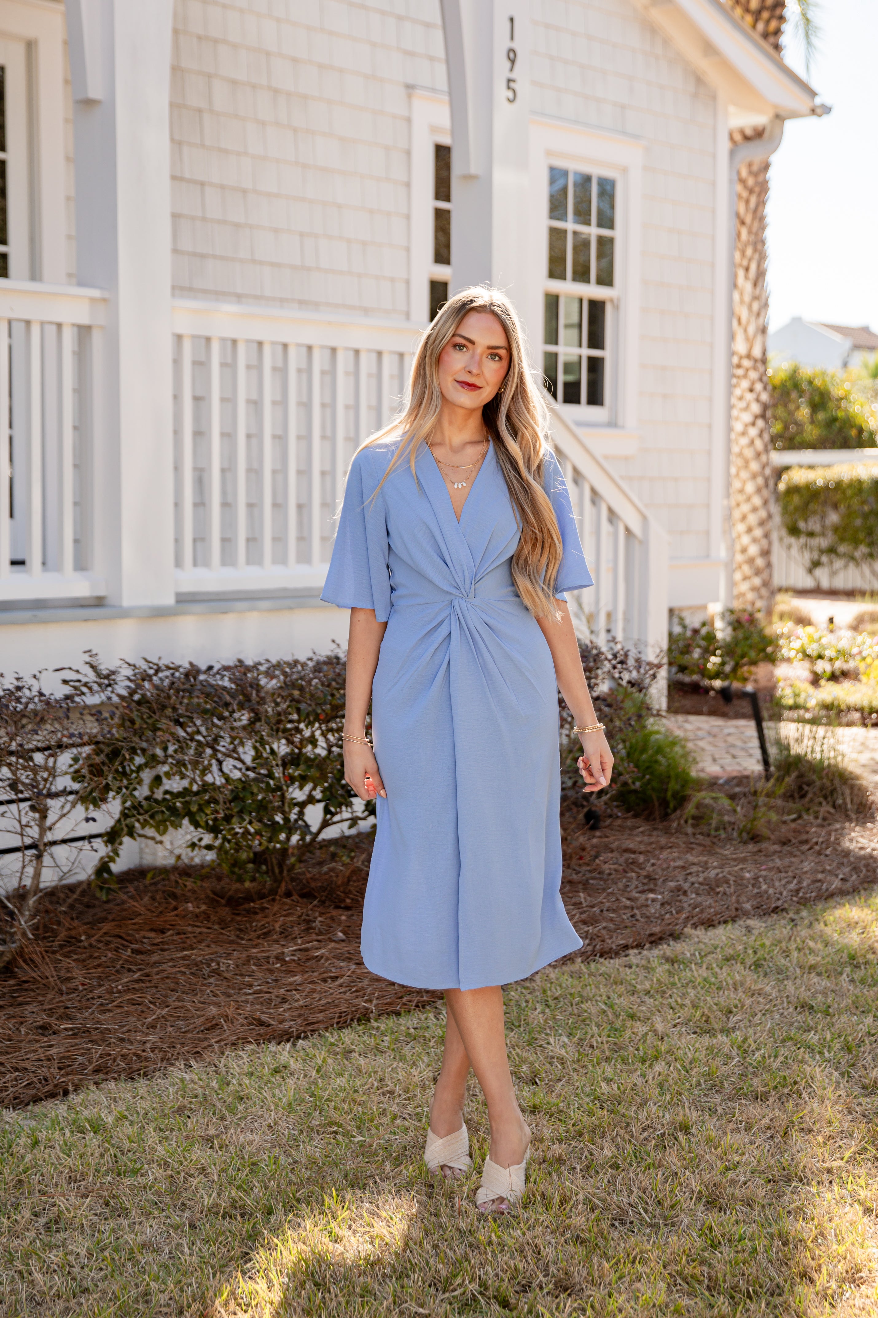 Woman in a light blue dress standing in front of a house.