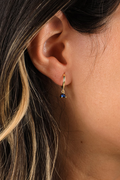 Close-up of an ear wearing a gold hoop earring with a blue gemstone.
