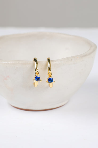 Gold earrings with blue gemstones on a white surface
