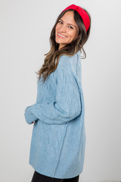 Woman wearing a blue cable knit sweater and red headband on a white background