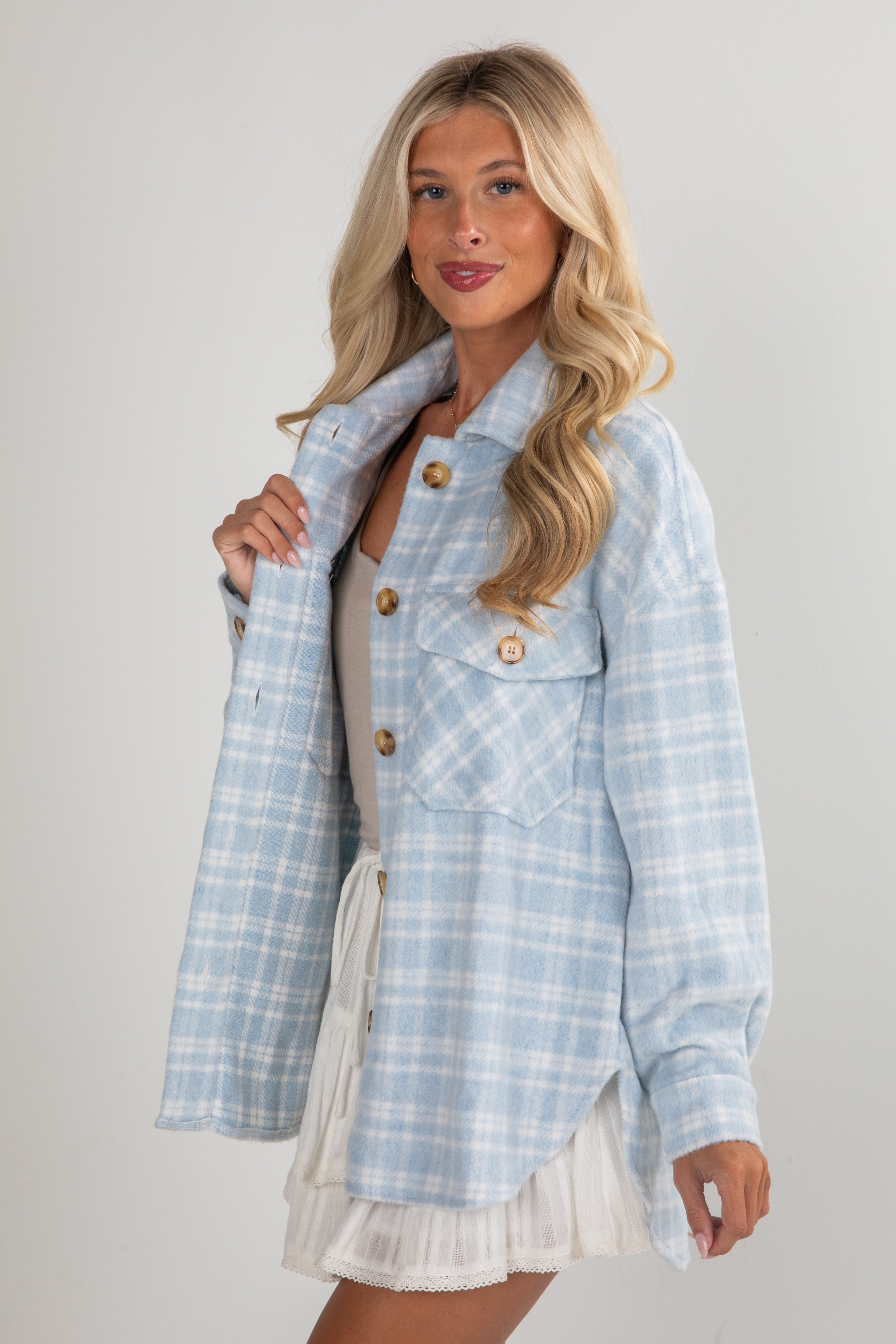 Woman wearing a light blue plaid jacket over a white dress on a gray background