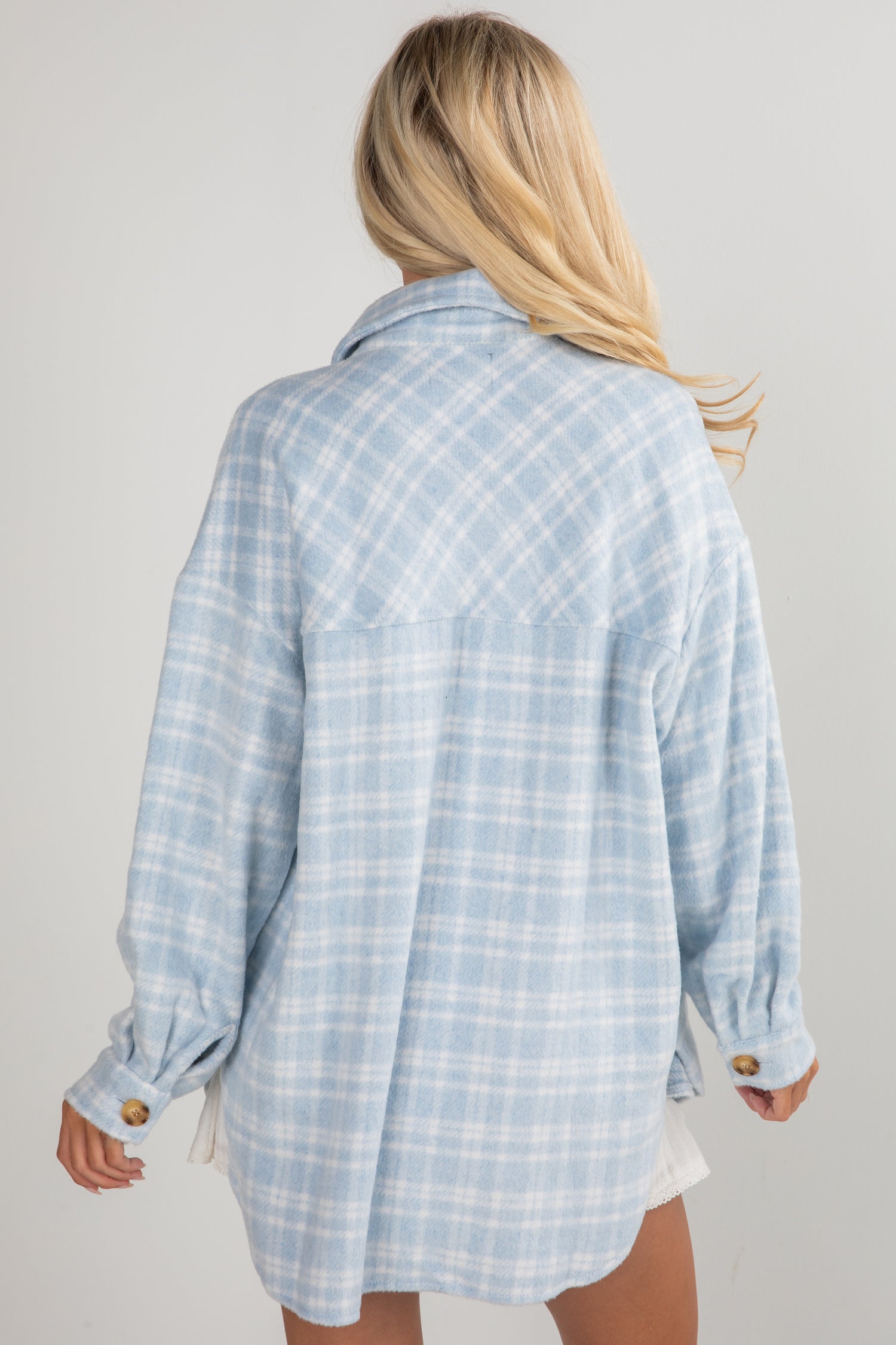 Person wearing a light blue plaid shirt on a plain background