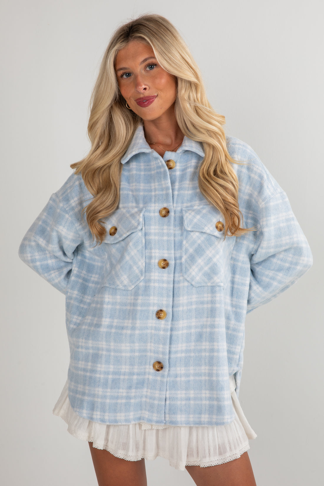 Woman wearing a light blue plaid jacket with wooden buttons on a plain background