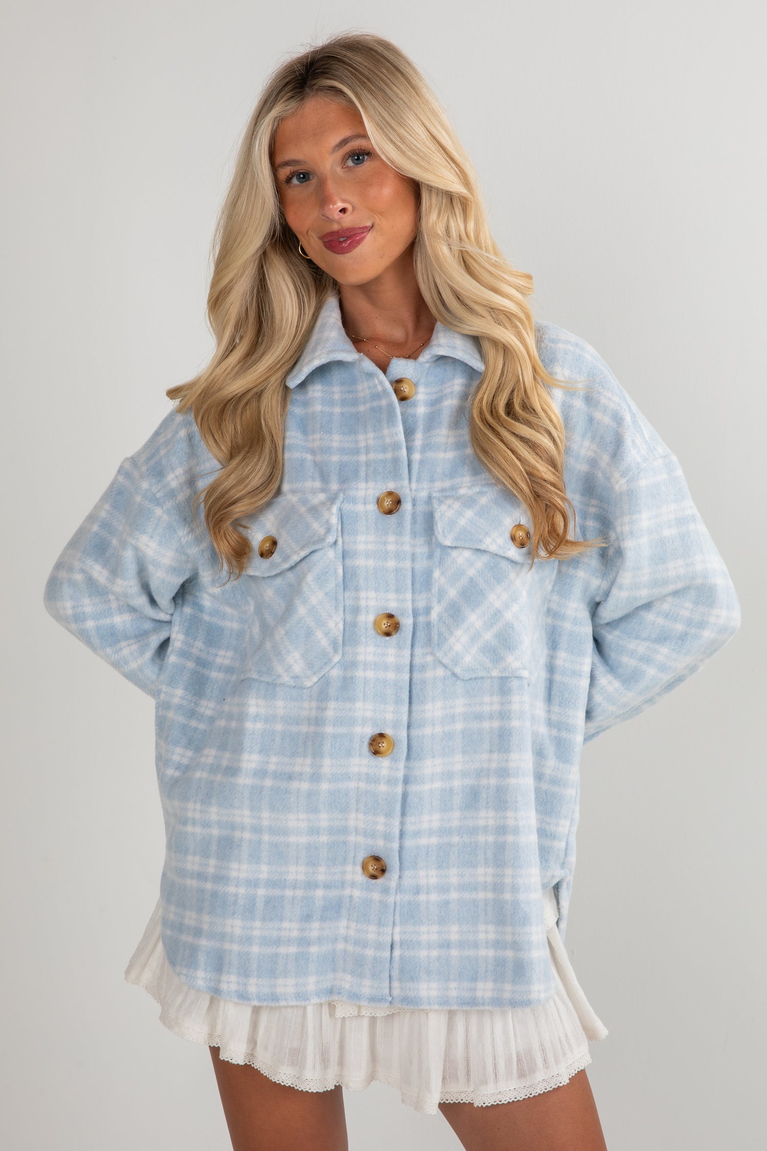 Woman wearing a light blue plaid jacket with wooden buttons on a plain background
