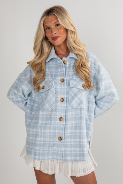 Woman wearing a light blue plaid jacket with wooden buttons on a plain background
