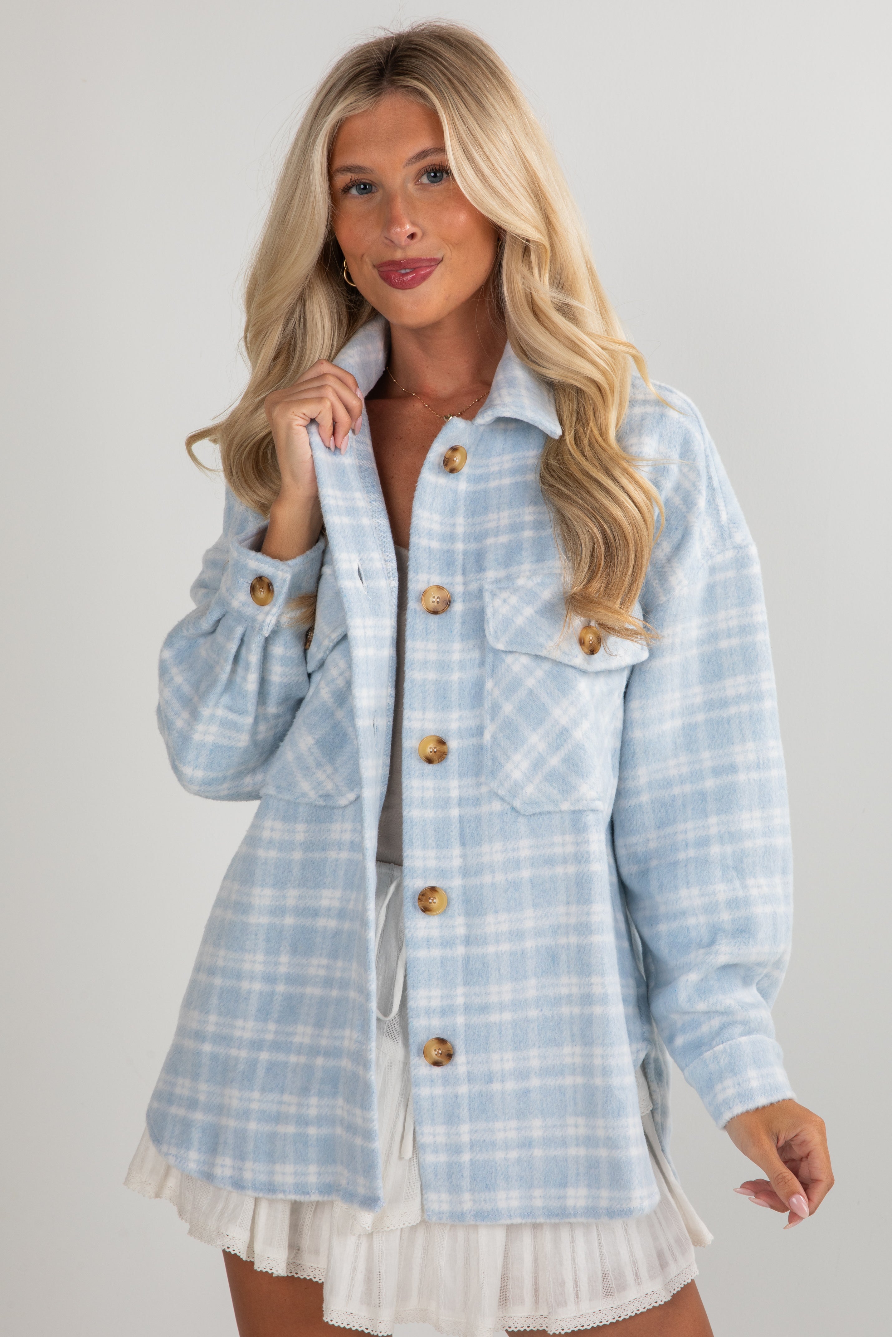 Woman wearing a light blue plaid jacket over a white dress on a plain background