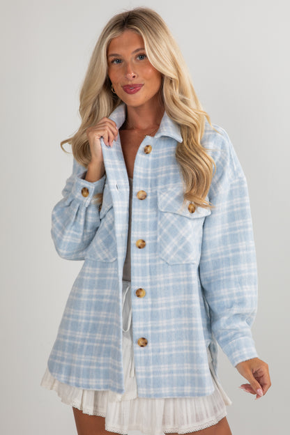 Woman wearing a light blue plaid jacket over a white dress on a plain background