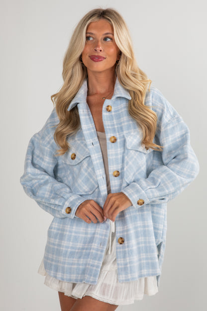 Woman wearing a light blue plaid jacket with gold buttons on a plain background