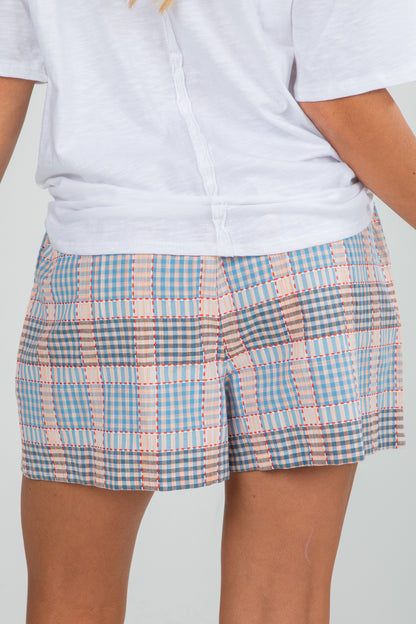 Person wearing a white shirt and blue plaid shorts on a plain background