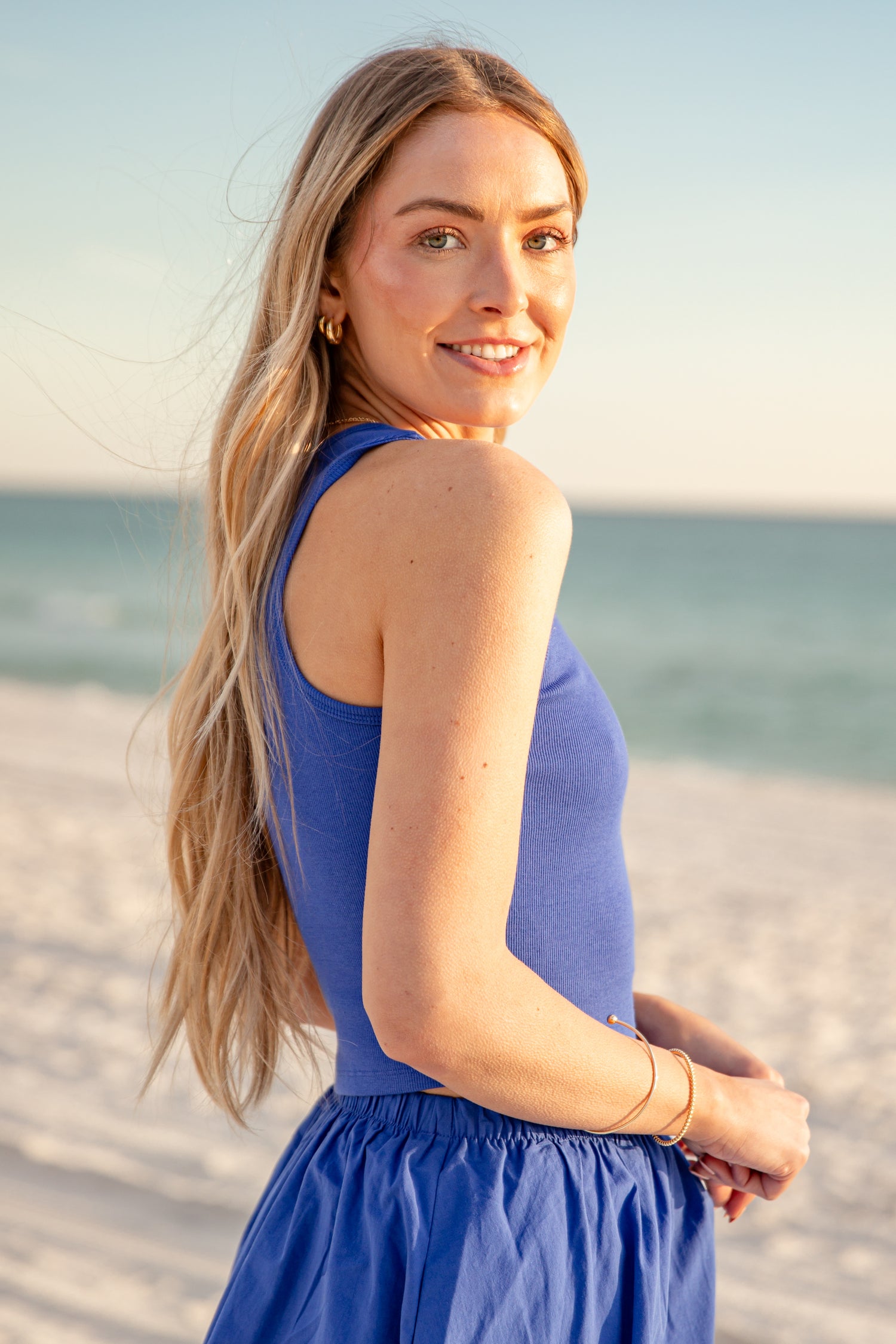 Woman in a blue top standing on a beach with ocean in the background