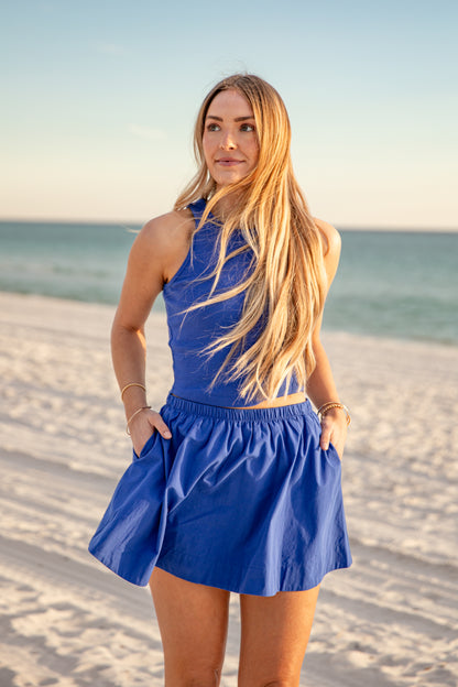 Woman in a blue dress standing on a beach with ocean in the background