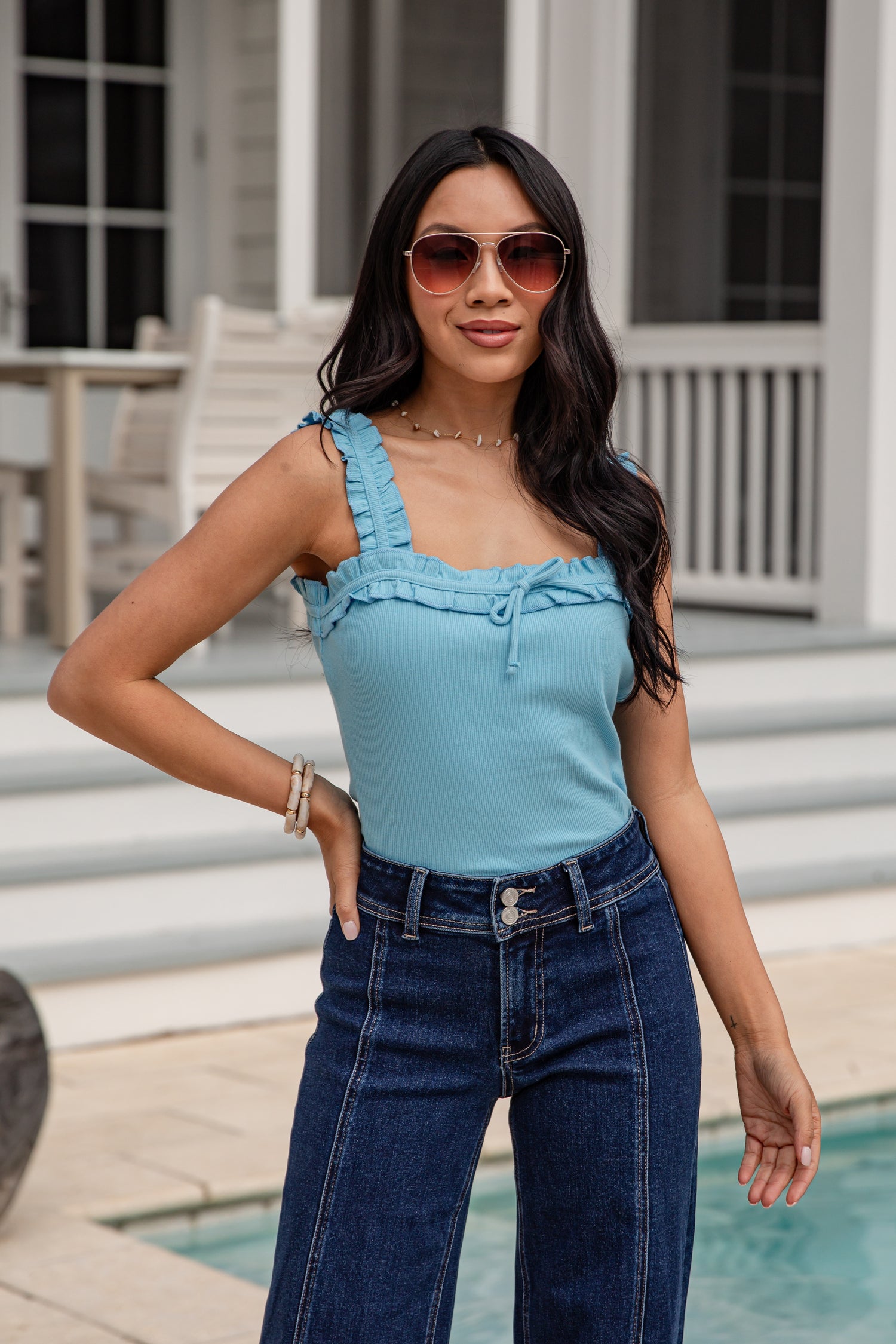 Woman wearing a blue top and jeans standing by a pool.
