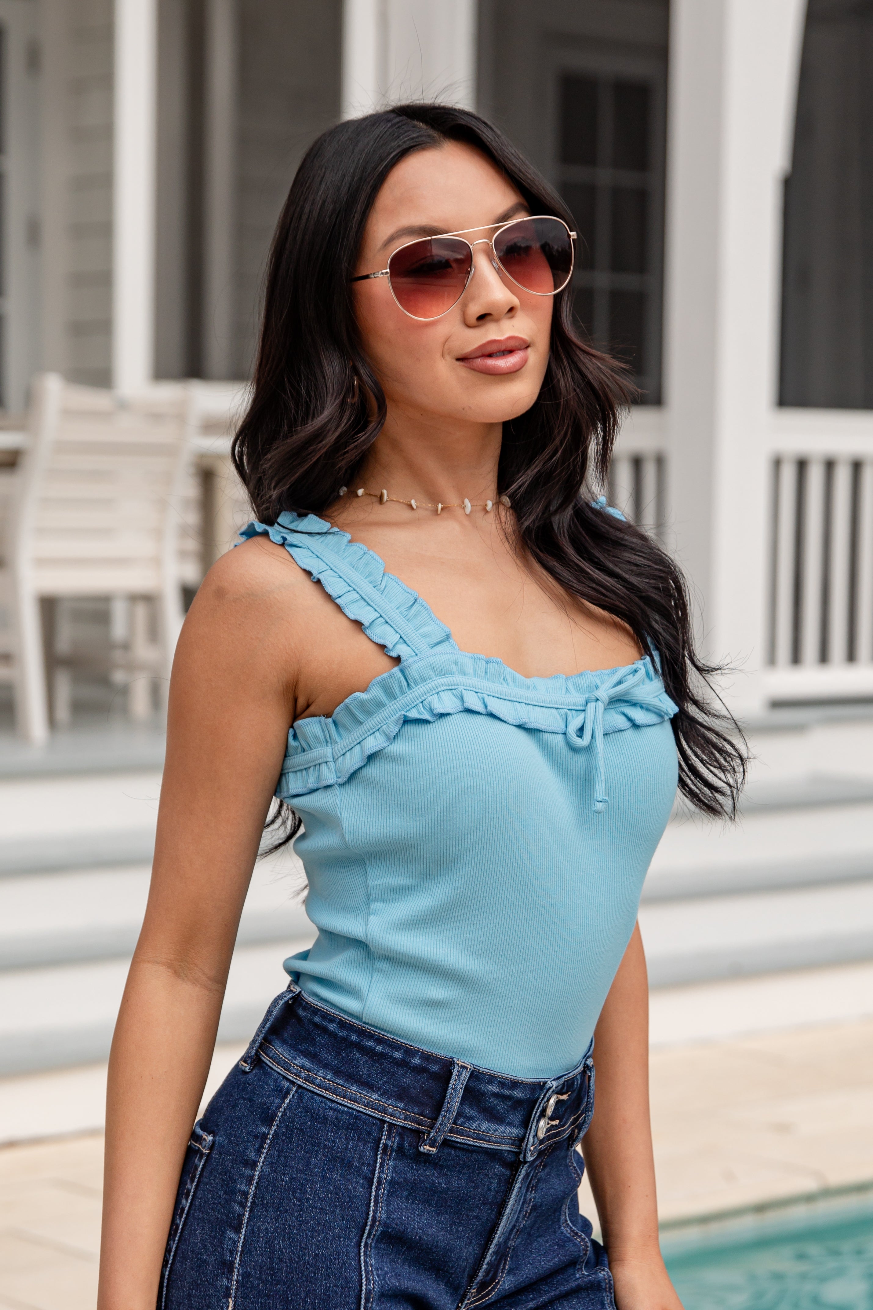 Woman wearing a light blue top and dark blue jeans with sunglasses outdoors.