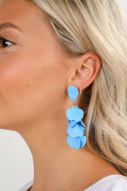 Close-up of a person wearing blue floral earrings with a neutral background