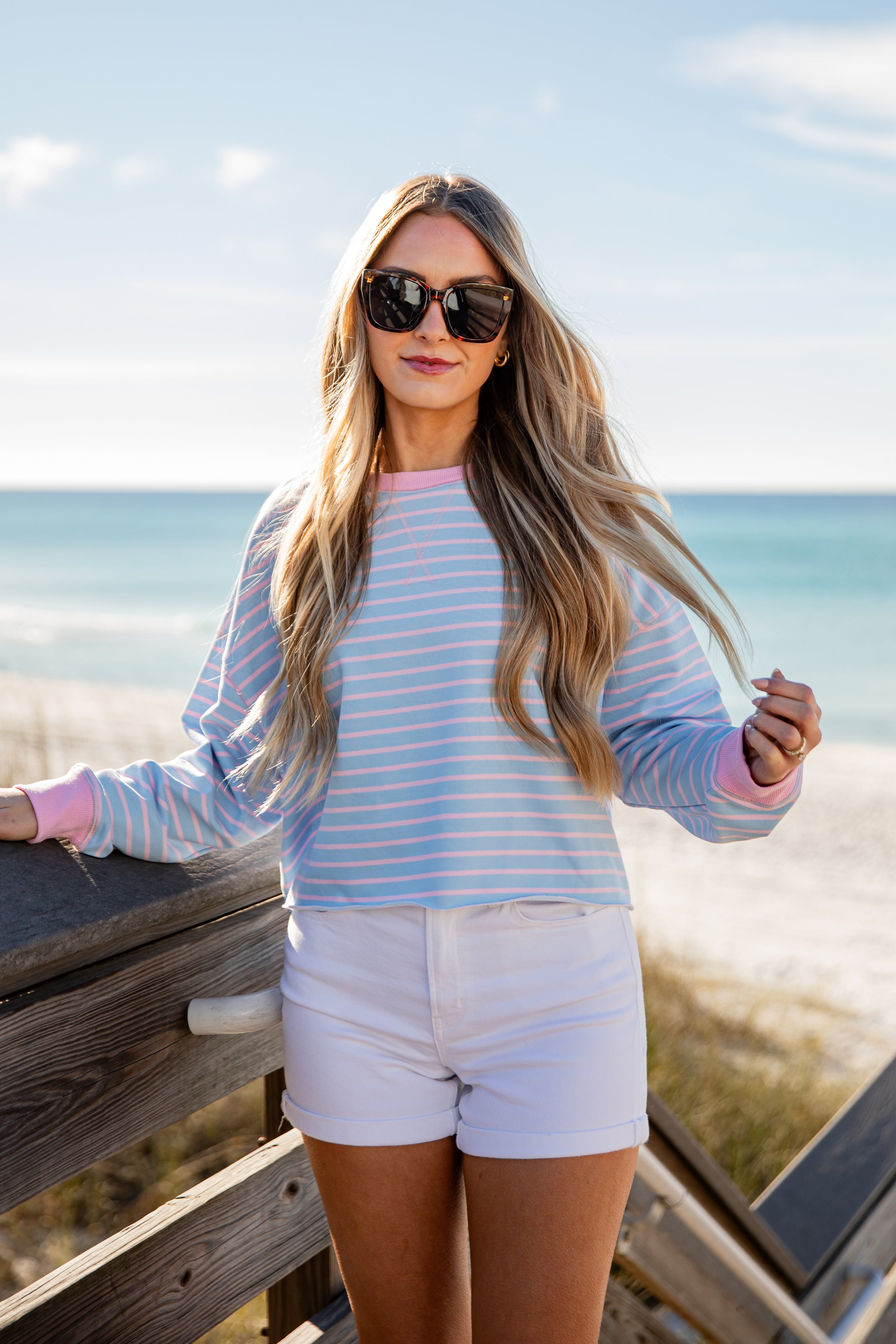 Woman in a striped shirt and shorts standing on a wooden deck by the ocean.