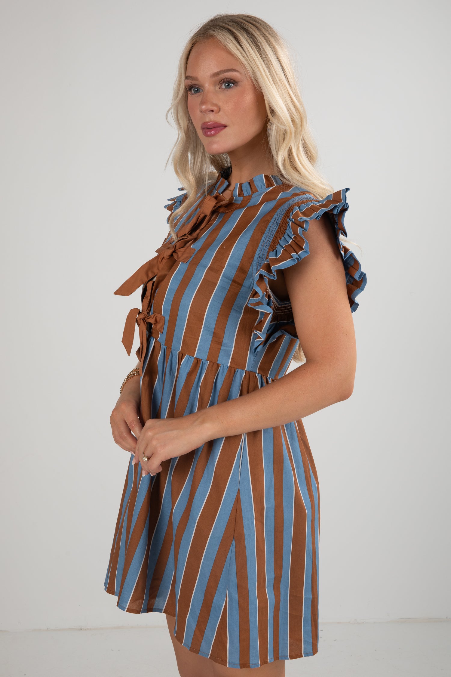 Woman wearing a brown and blue striped dress with ruffled sleeves against a white background