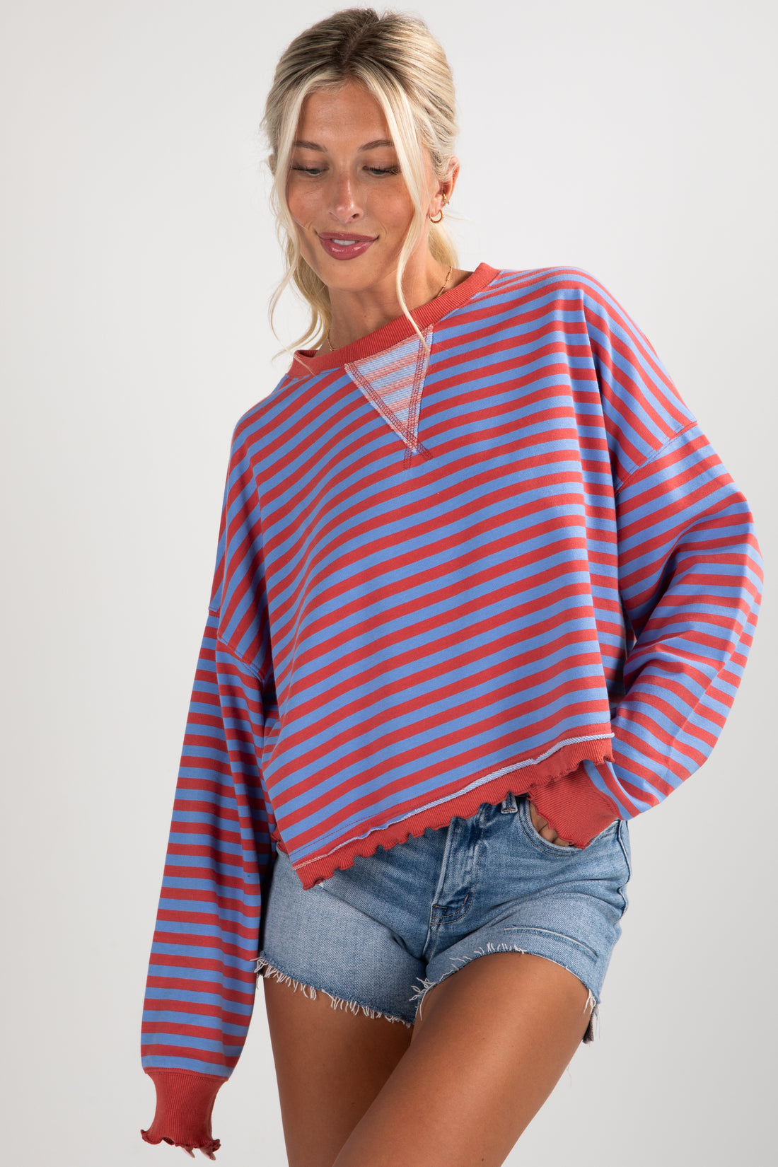 Woman wearing a red and blue striped sweater with denim shorts on a white background
