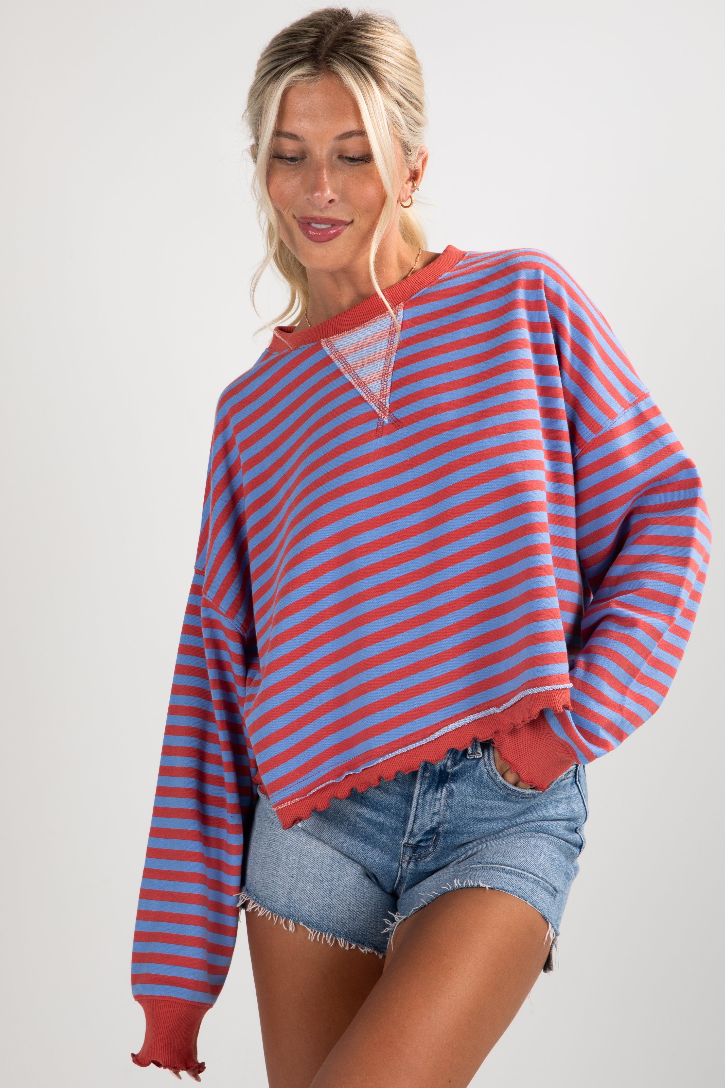 Woman wearing a red and blue striped sweater with denim shorts on a white background