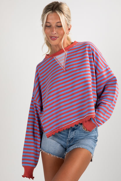Woman wearing a red and blue striped sweater with denim shorts on a white background