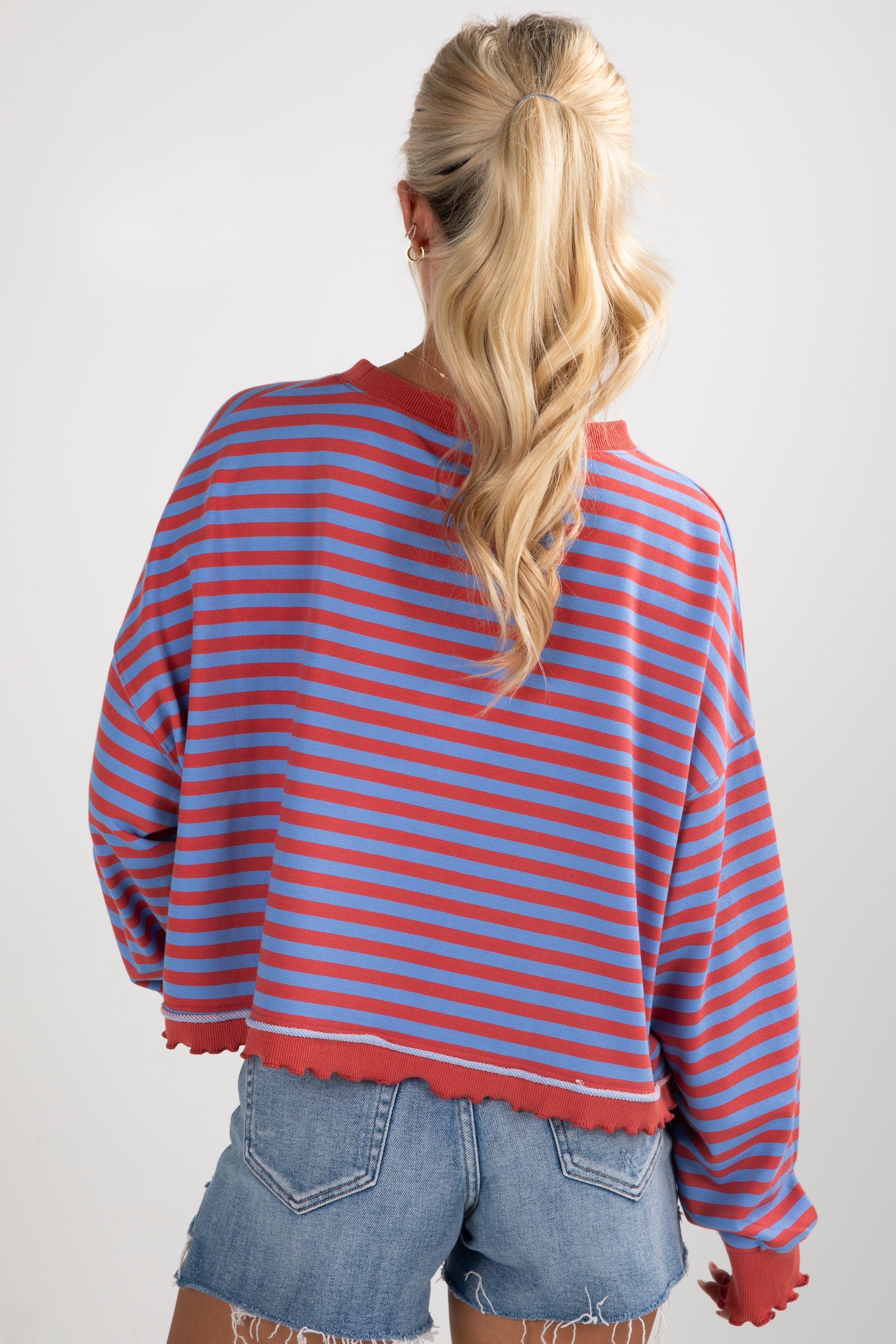 Person wearing a red and blue striped sweater with denim shorts on a plain background