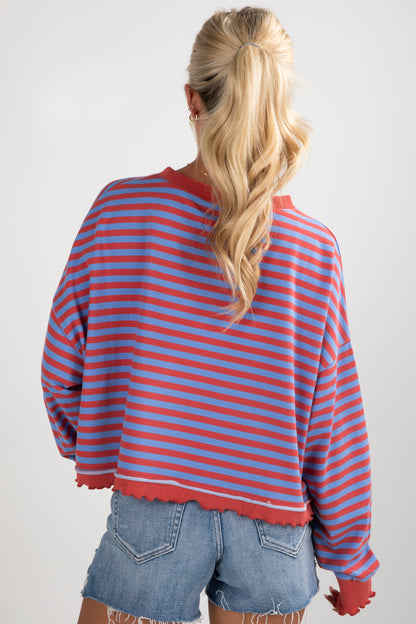 Person wearing a red and blue striped sweater with denim shorts on a plain background