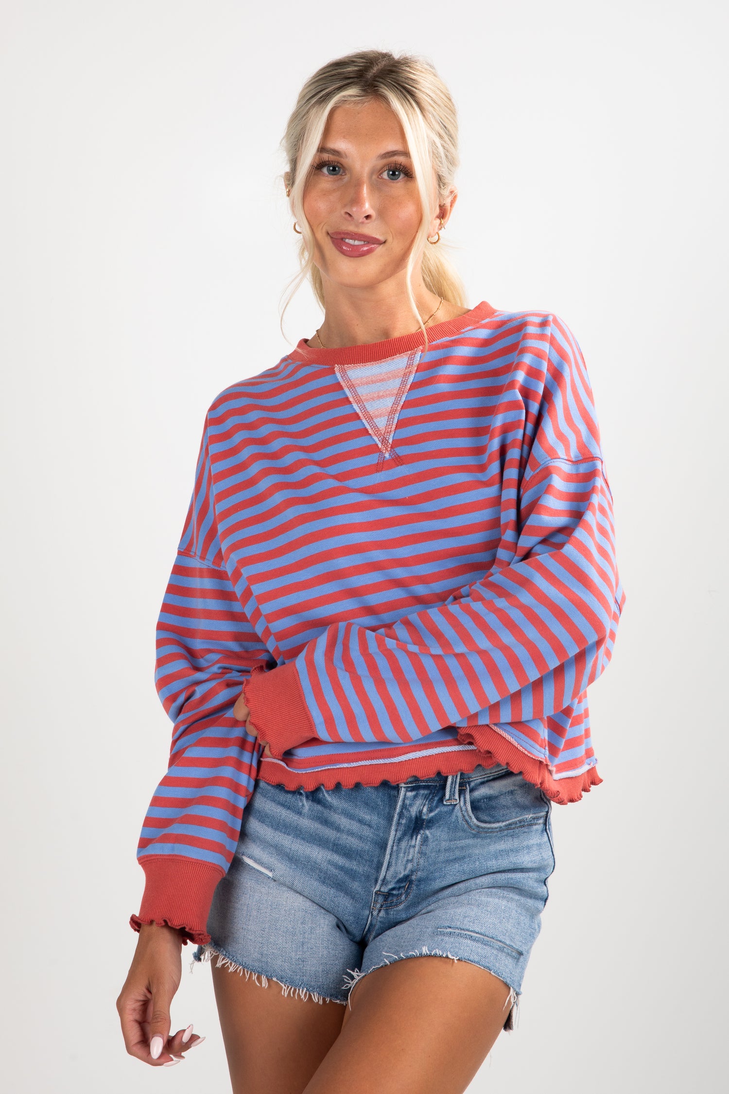 Woman wearing a red and blue striped sweater with denim shorts on a white background