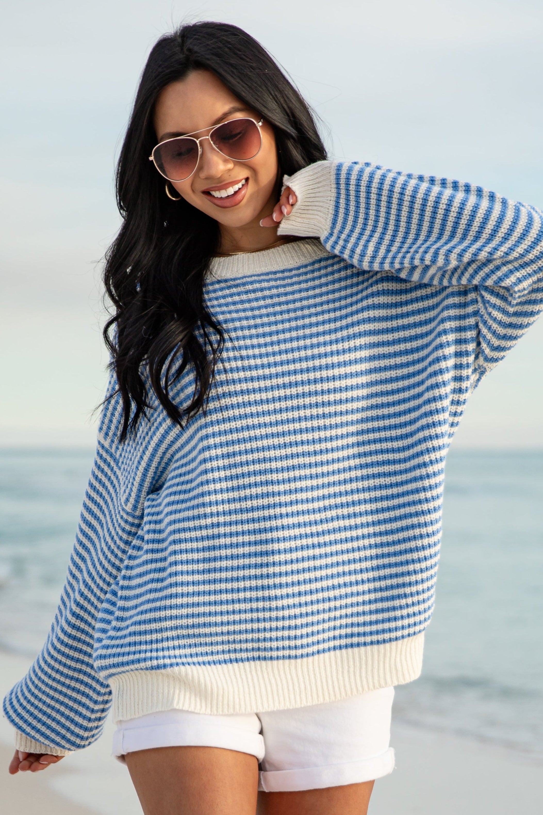 Woman wearing a blue and white striped sweater and white shorts on a beach.