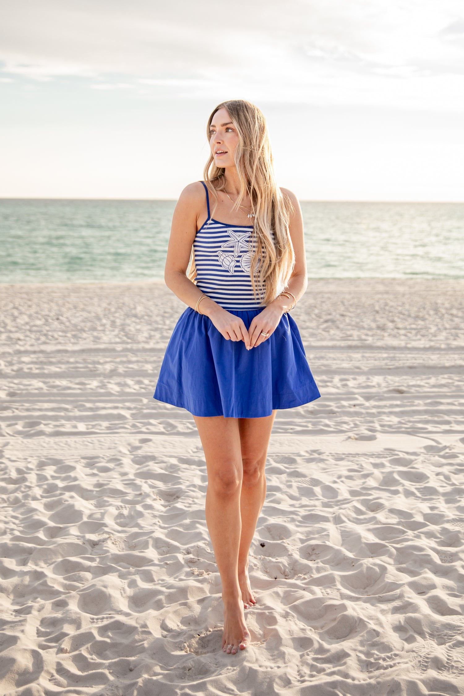 Woman in a blue dress standing on a sandy beach with ocean in the background