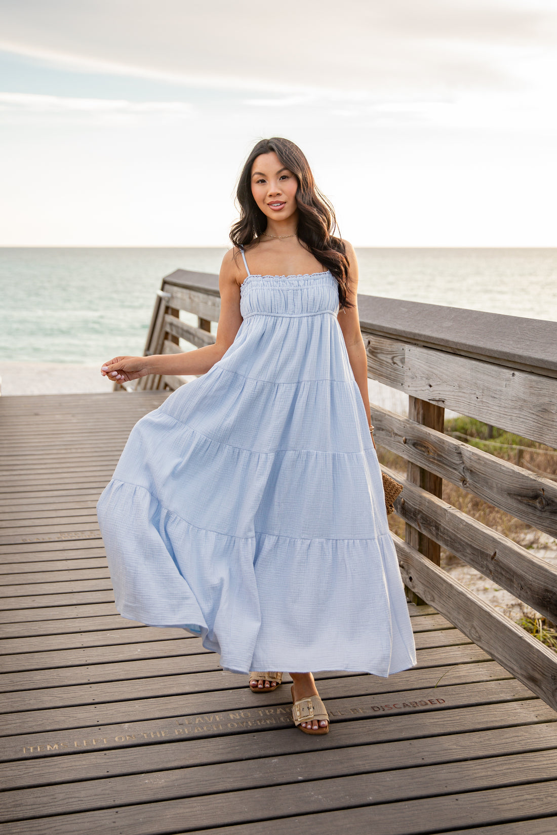Woman in a light blue dress standing on a wooden pier by the ocean.