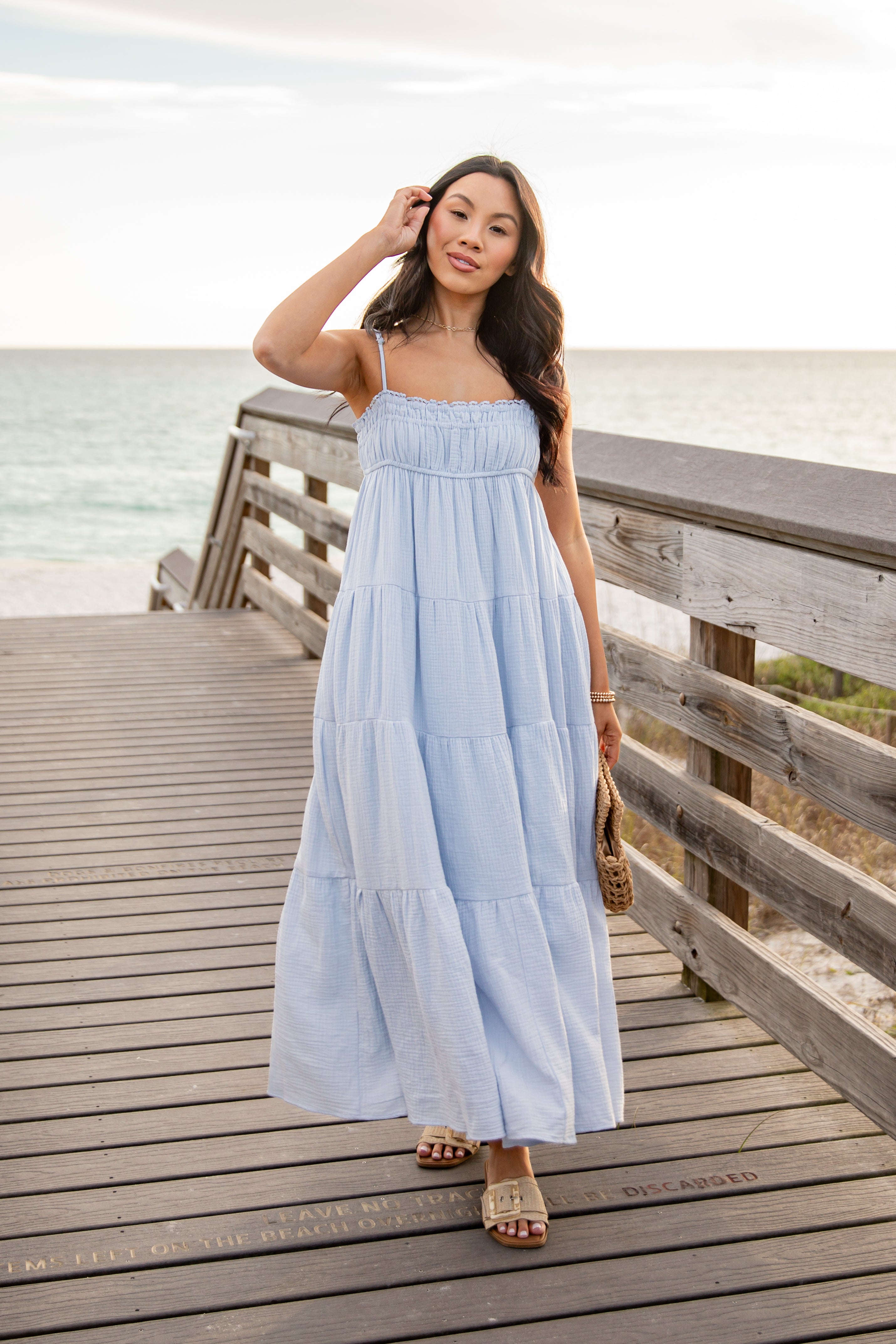 Woman in a light blue dress standing on a wooden pier by the ocean.