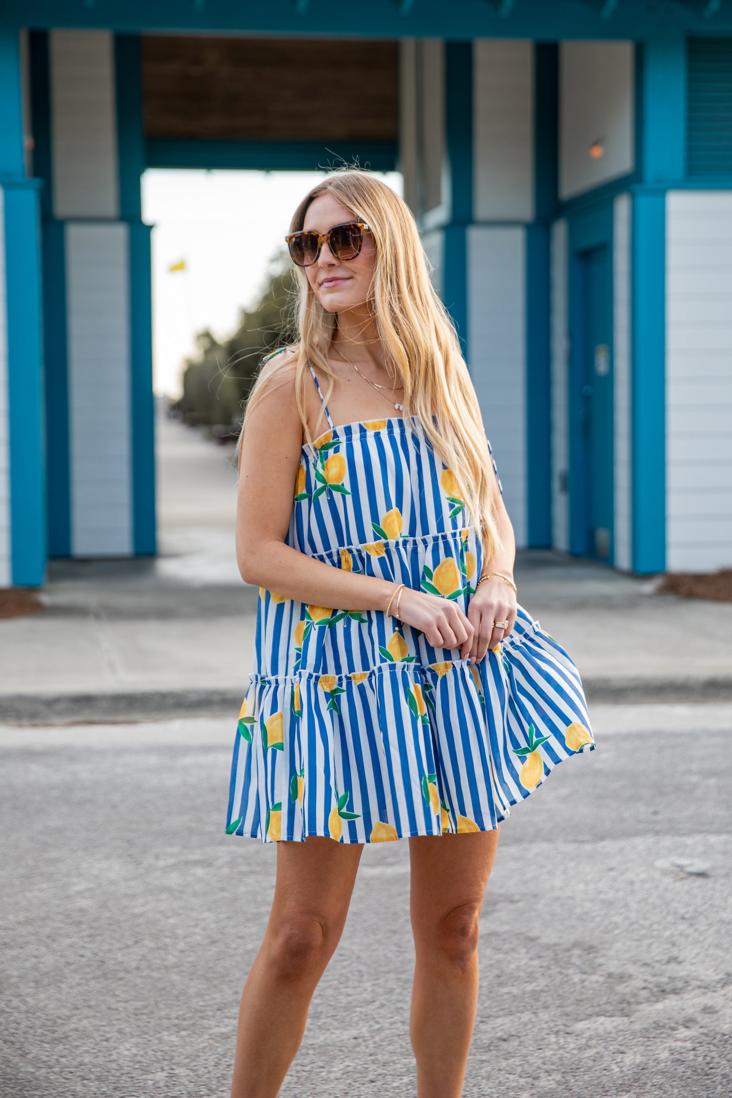 Woman wearing a blue and white striped dress with yellow accents in front of a beach hut.