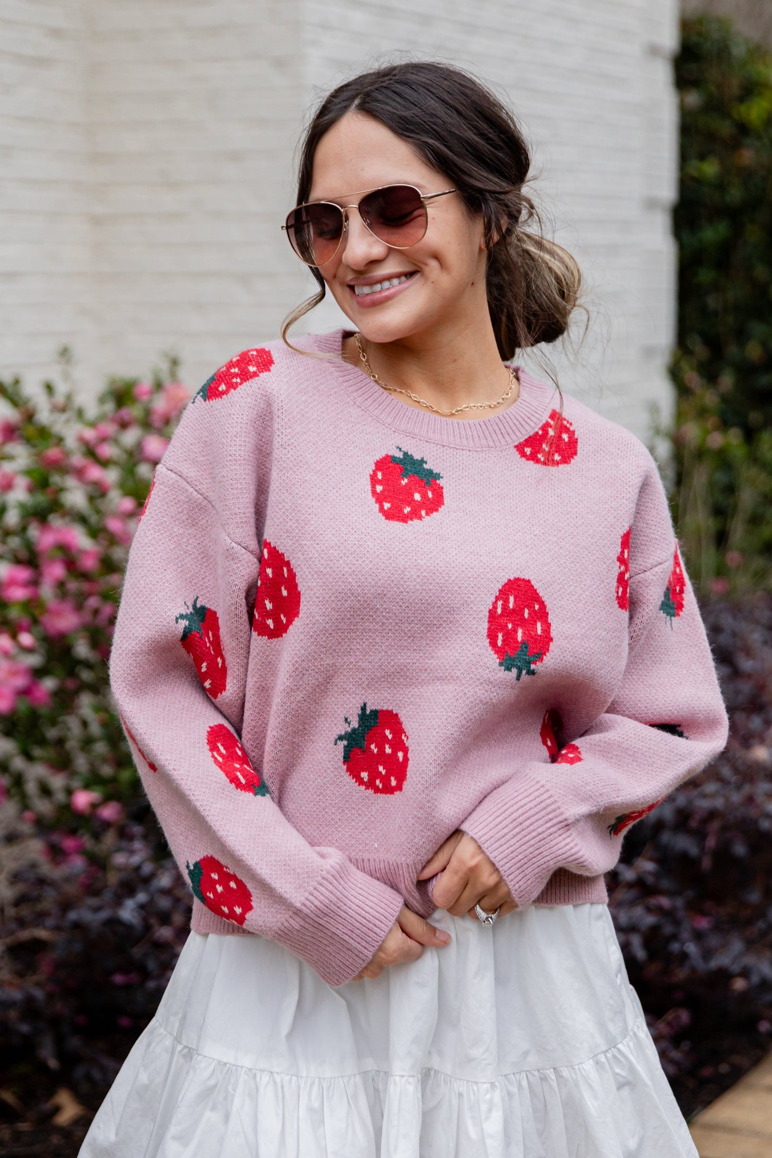 Woman wearing a pink sweater with strawberry patterns outdoors.